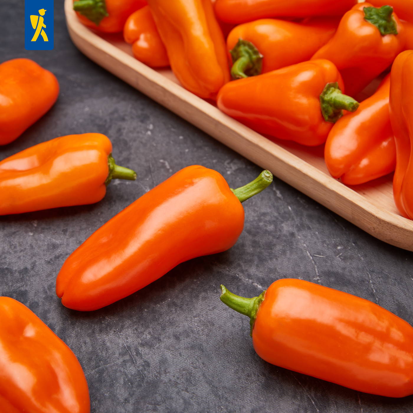 Mehrere orange Paprika, einige auf einem schwarzen Steinuntergrund, andere in einer Holzschale.