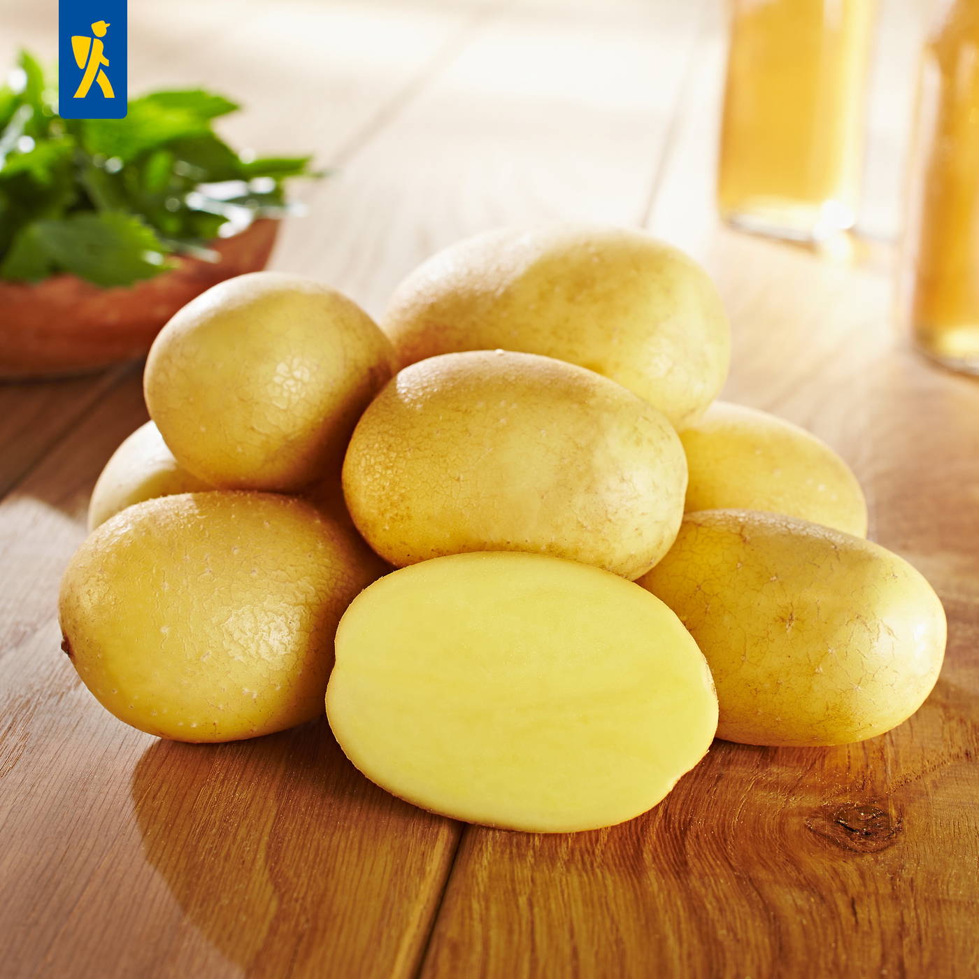 Mehrere gelbe Kartoffeln auf einer Holzfläche, eine halbierte Kartoffel zeigt das Innere.