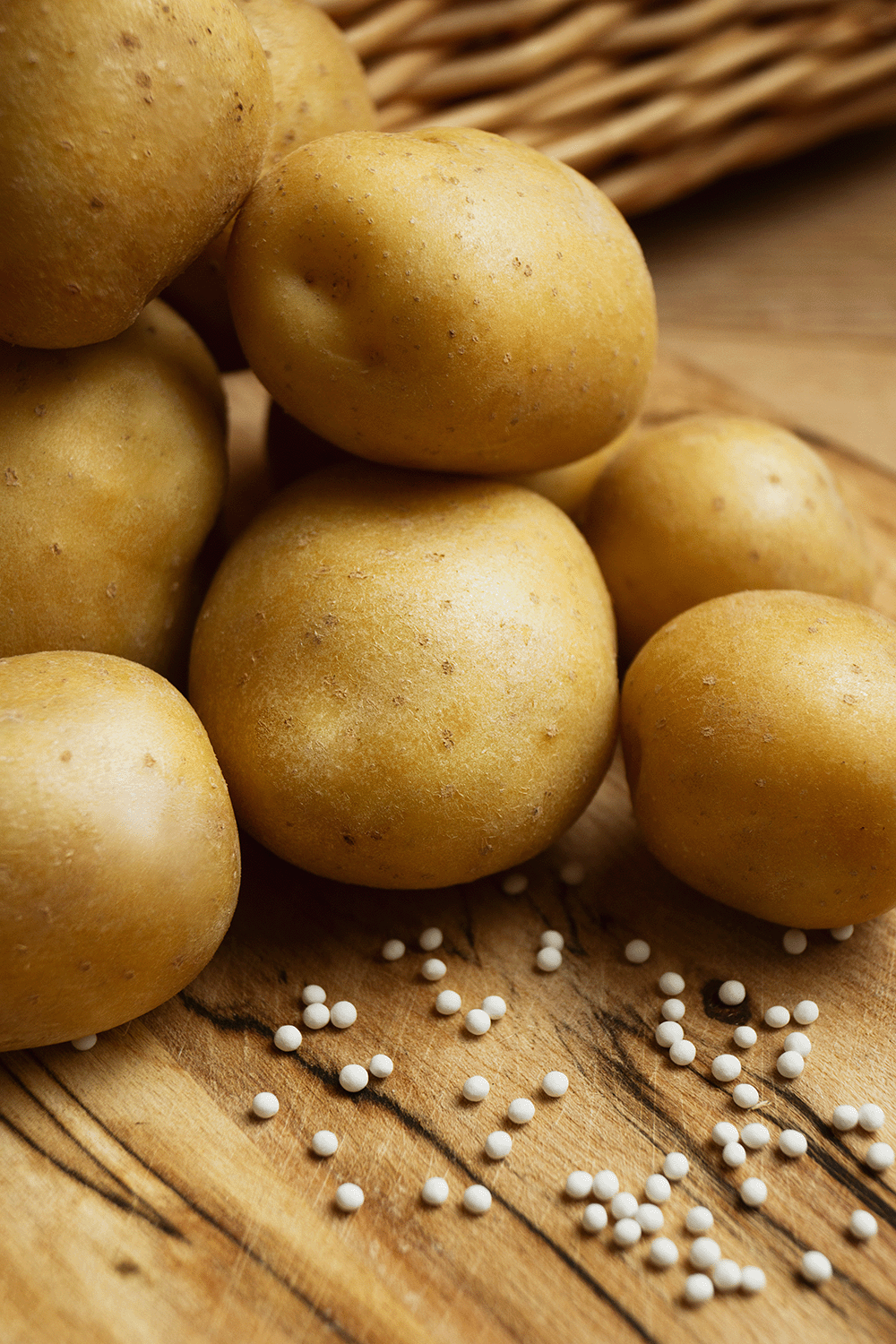 Mehrere kleine, runde, gelbe Kartoffeln liegen auf einem Holztisch, darunter sind weiße Senfsamen verstreut.
