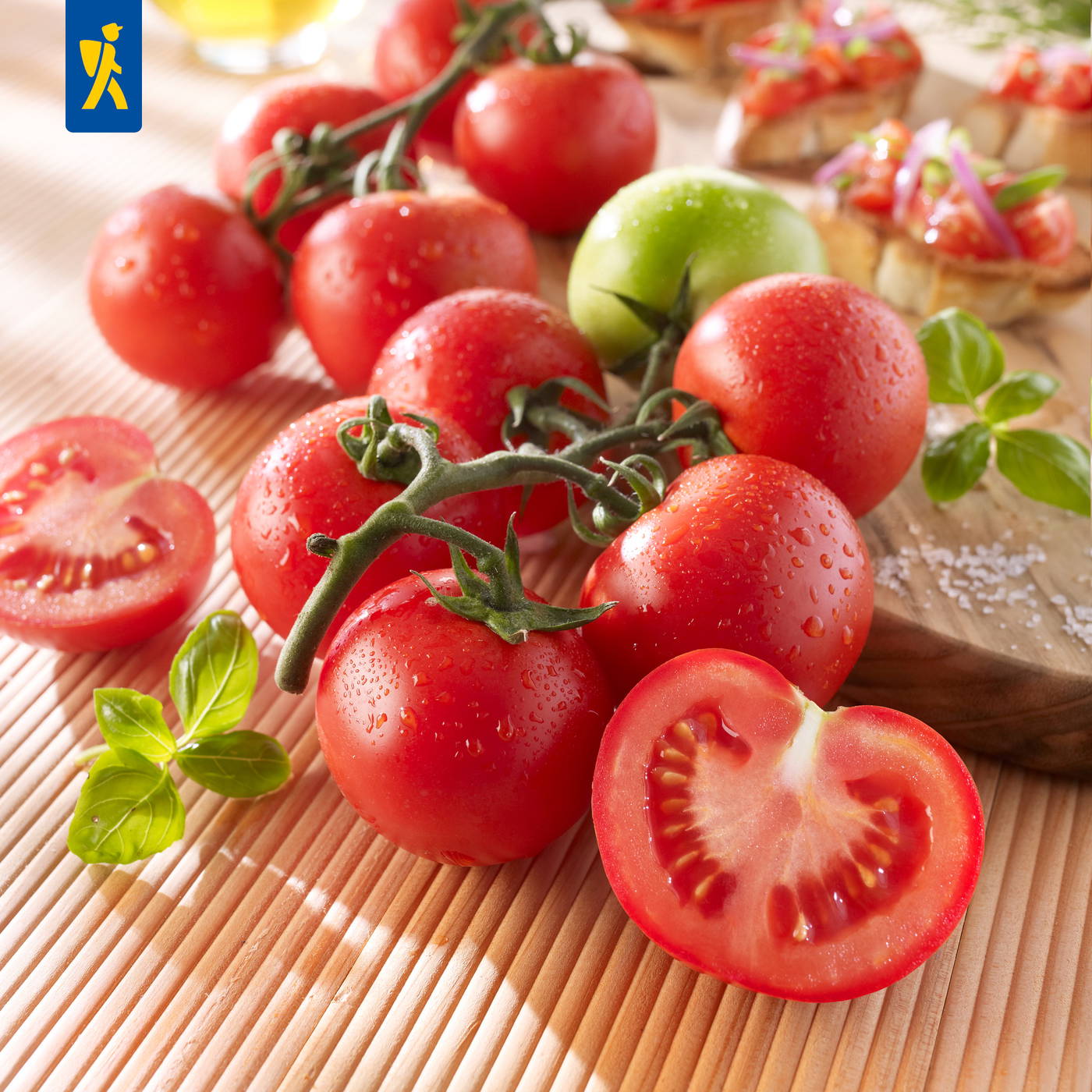 Rote Tomaten auf einem Bambusmatte mit einer halbierten Tomate, frischen Basilikumblättern und Wassertröpfchen.