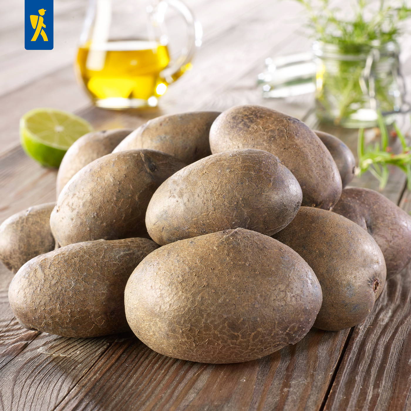 Mehrere Kartoffeln auf einem Holztisch mit Zitronen, Öl und Kräutern im Hintergrund.