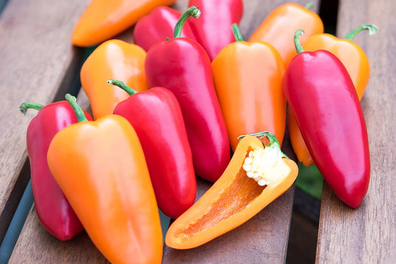 Bunte Paprika auf Holztablett, ein halbierter Paprika zeigt Innenseite.