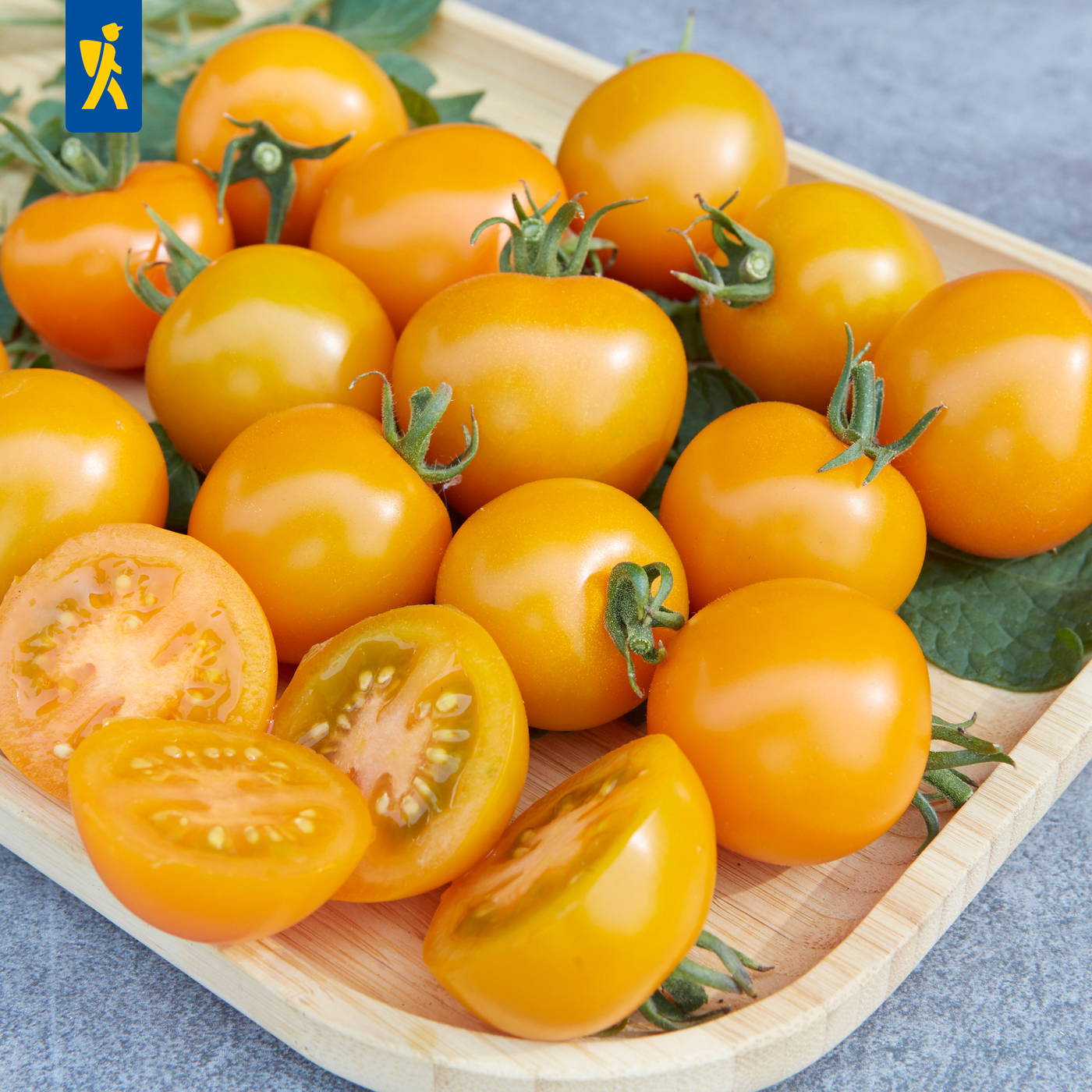 Gelbe Tomaten auf einem Holztablett, einige halbiert, mit grünen Blättern.