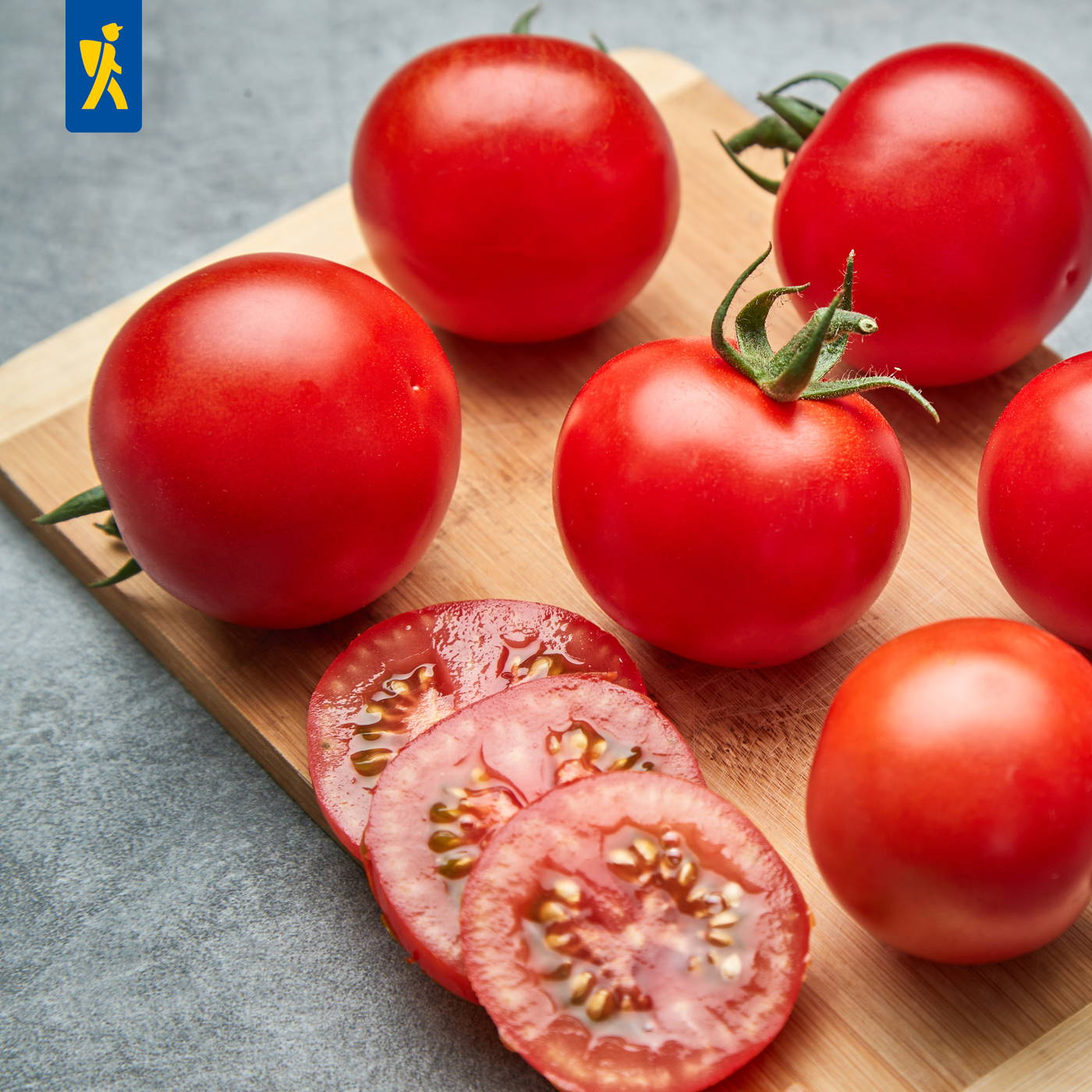 Rote Tomaten auf einem Holzbrett, einige in Scheiben geschnitten, vor grauem Hintergrund.