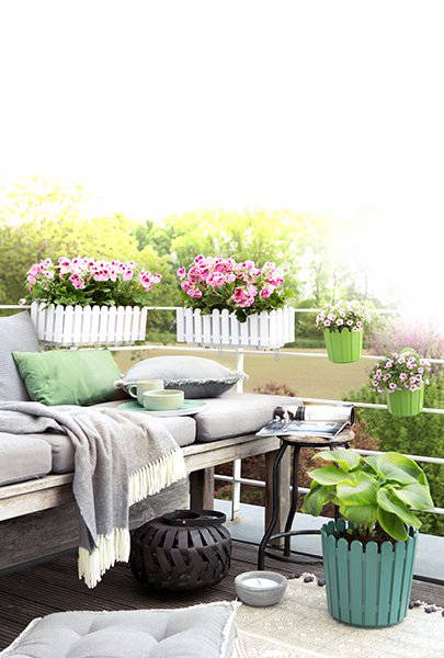 Balkon mit Gartenpflanzen, sofa, Kissen und Decke, Tasse und Buch.