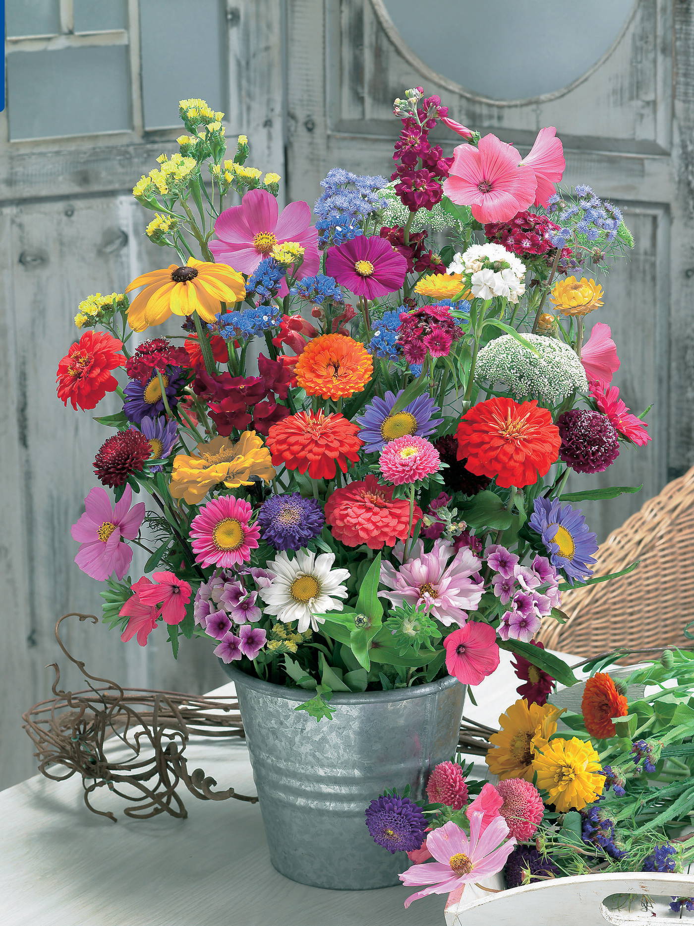Bunte Blumenmischung in einem Metalltopf auf einem Tisch vor einer Holzpaneelwand.