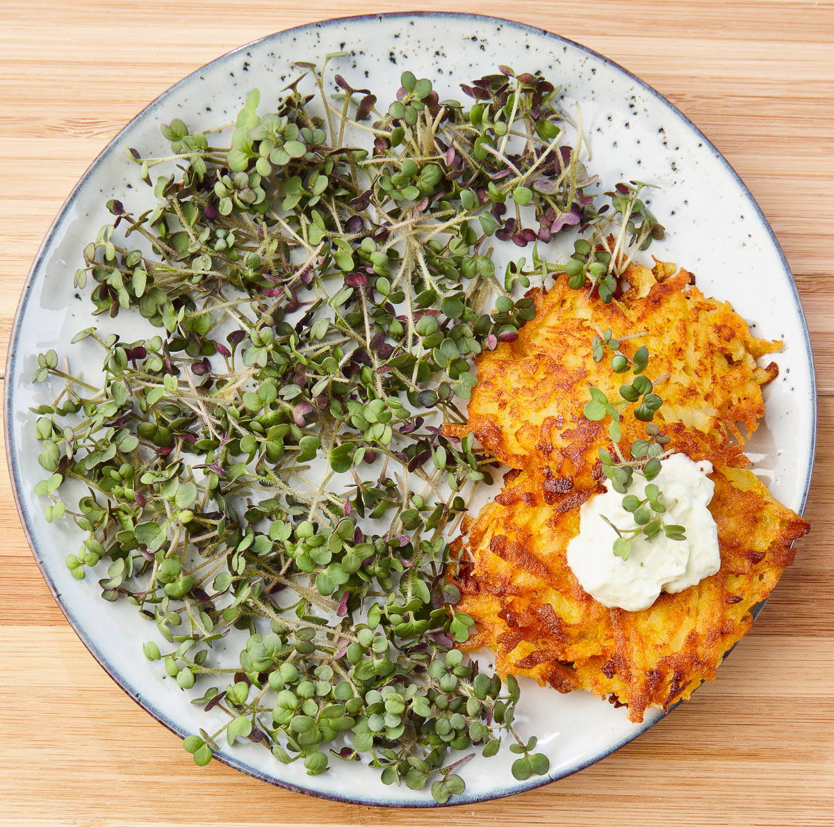 Kartoffelrösti mit Kräutern und grünem Sproß auf weißem Teller auf Holz.