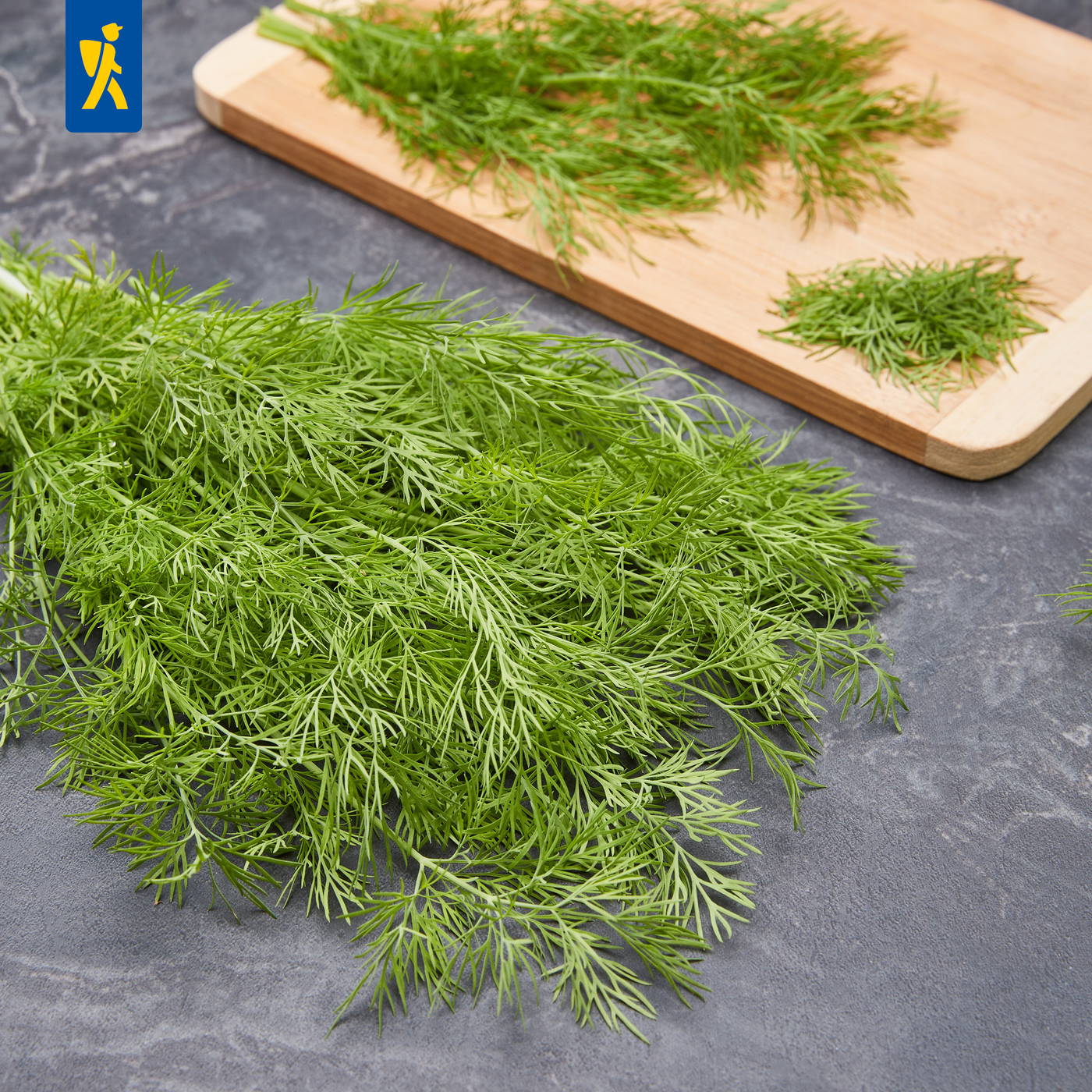 Haufen frischer, zart grüner Dill auf dunklem Steinuntergrund, mit weiteres Dill auf Schneidebrett im Hintergrund.
