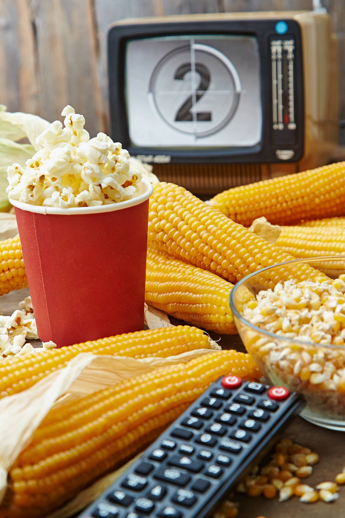 Maisskörner, Popcorn, Fernseher, Fernbedienung auf Holz.