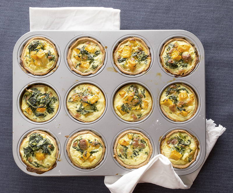 Miniquiches mit Spinat, Kürbis und Käse in einer Muffinform auf einem dunkelgrauen Tisch