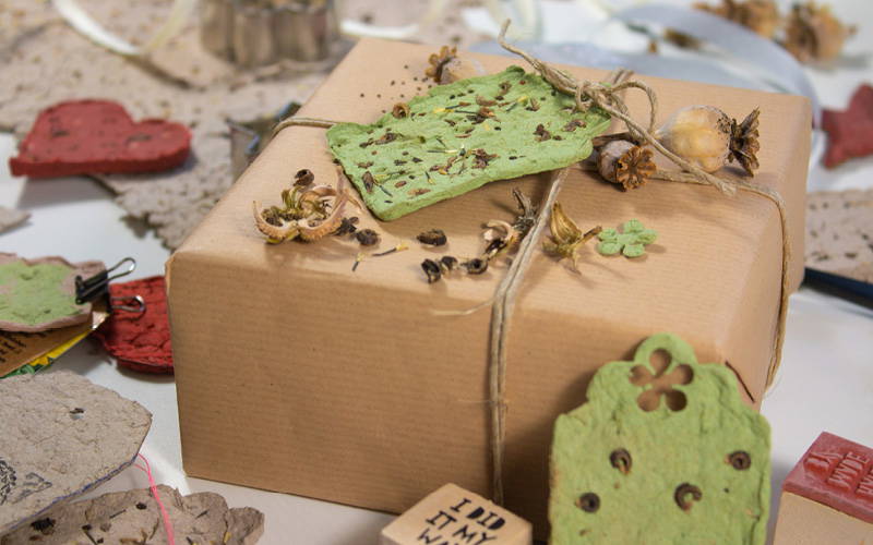 Paket mit grünem Blatt, getrockneten Pflanzen und kleinen Dekoteilen auf braunem Geschenkpapier.