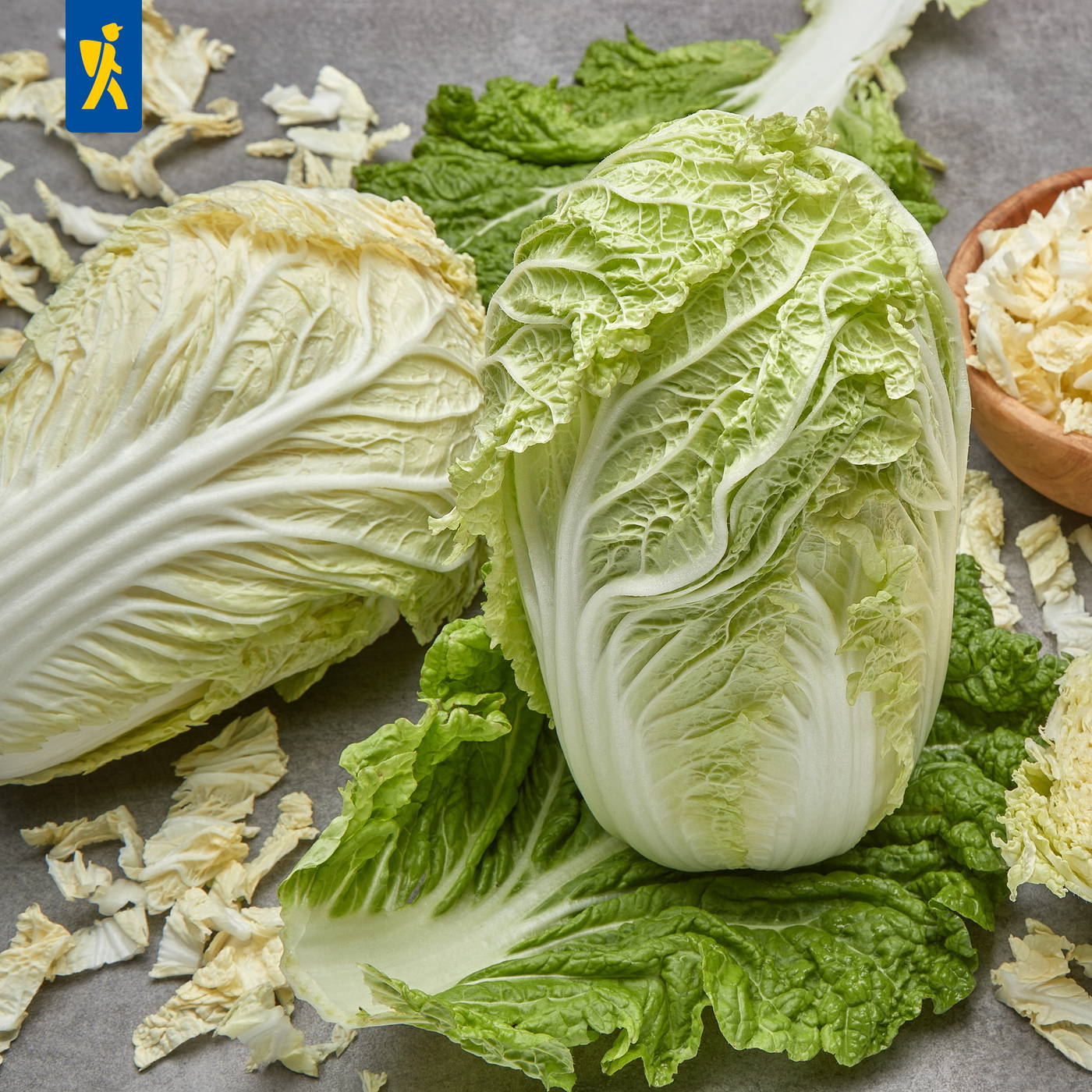 Zwei halbierte romaine Salatköpfe, umgeben von Blatt- und Rippenteilen, auf grauem Untergrund.