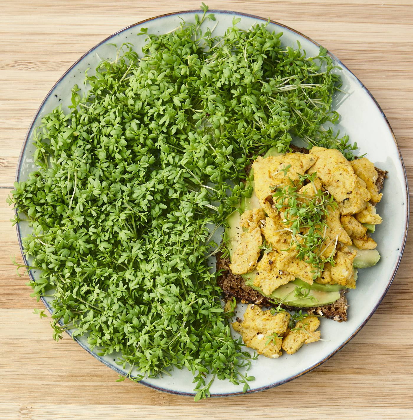 Schüssel mit Rührei, Avocado und viel frischem Kresse auf einem Holzbrett.