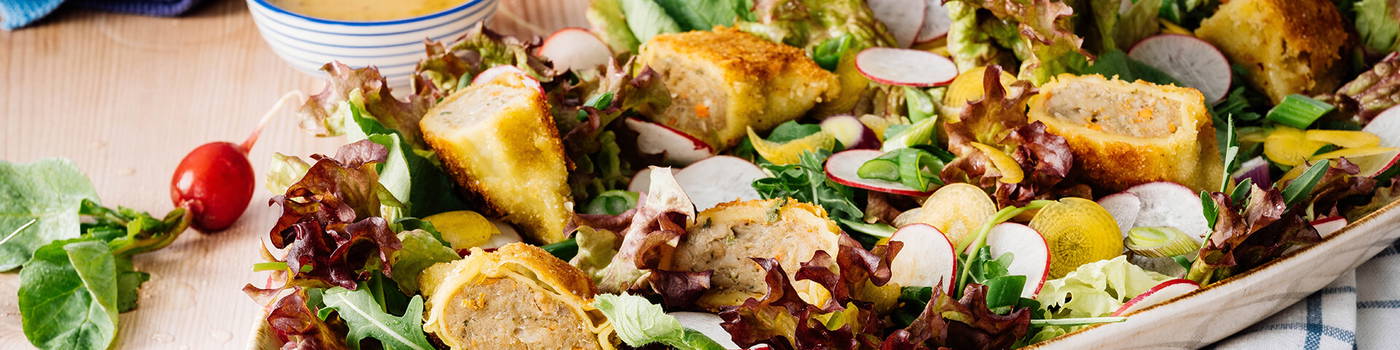 Gemüse mit panierten gefüllten Klößchen auf einem Salatbett in einer weißen Schüssel