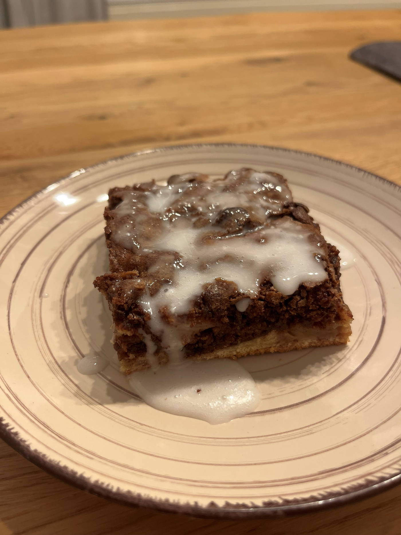 Kuchenstück mit Schokoladenstreuseln und Zuckerguss auf einer weißen gerippten Platte auf Holz.
