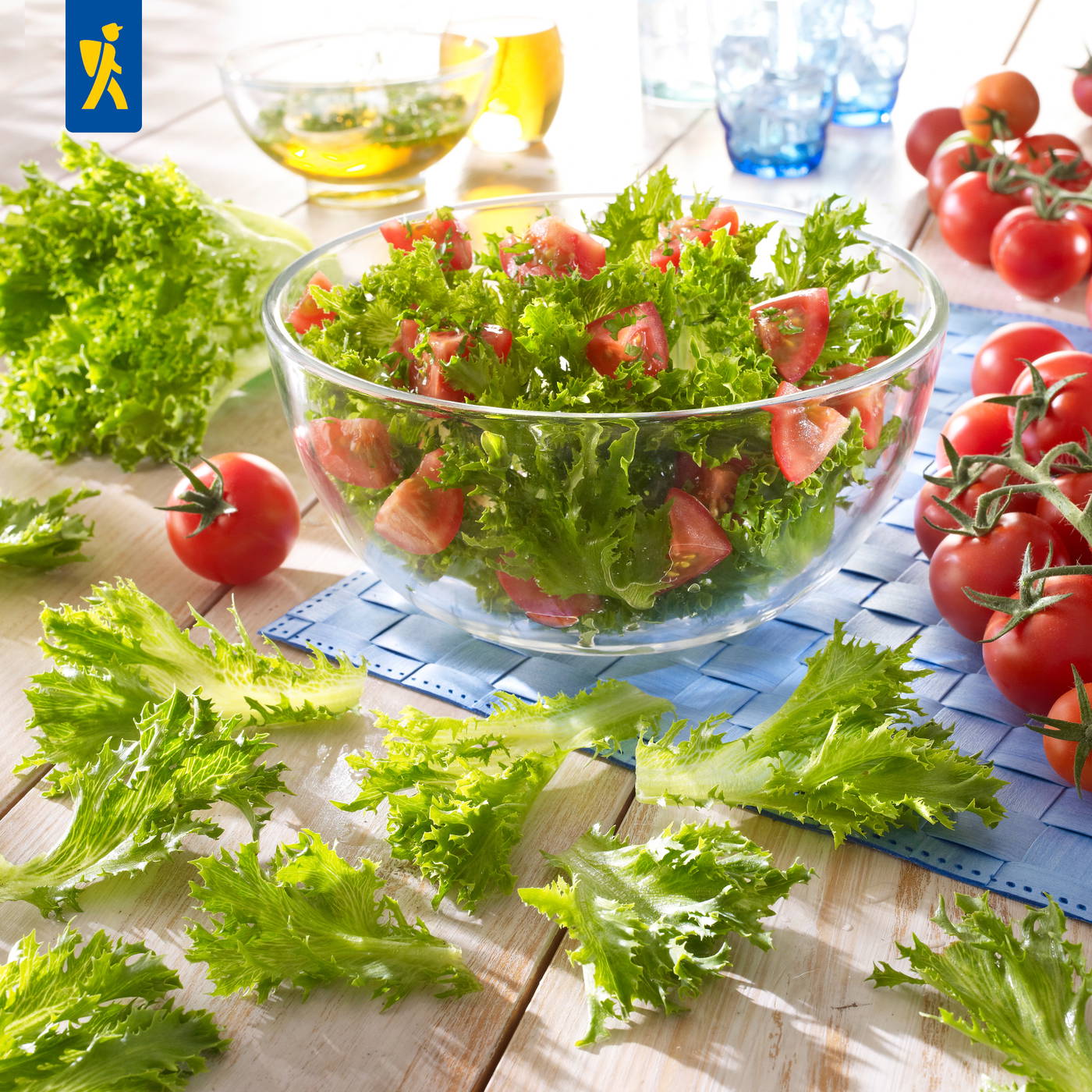 Schüssel mit gemischtem grünen Salat und Tomaten, weitere Tomaten und Salatblätter auf Holz Tisch.