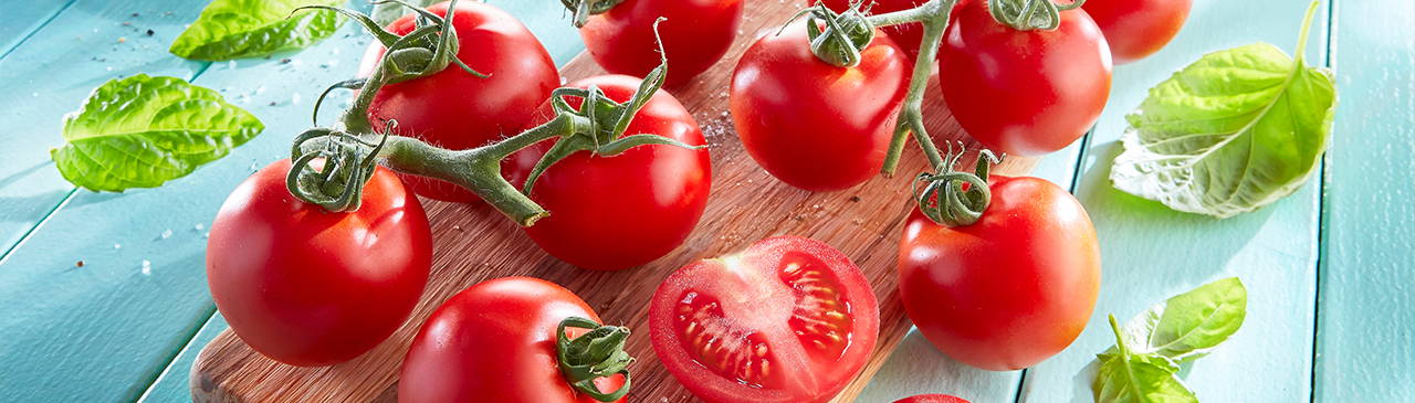 Mehrere Tomaten auf einem Brett mit grünen Blättern, einige Tomaten halbiert.