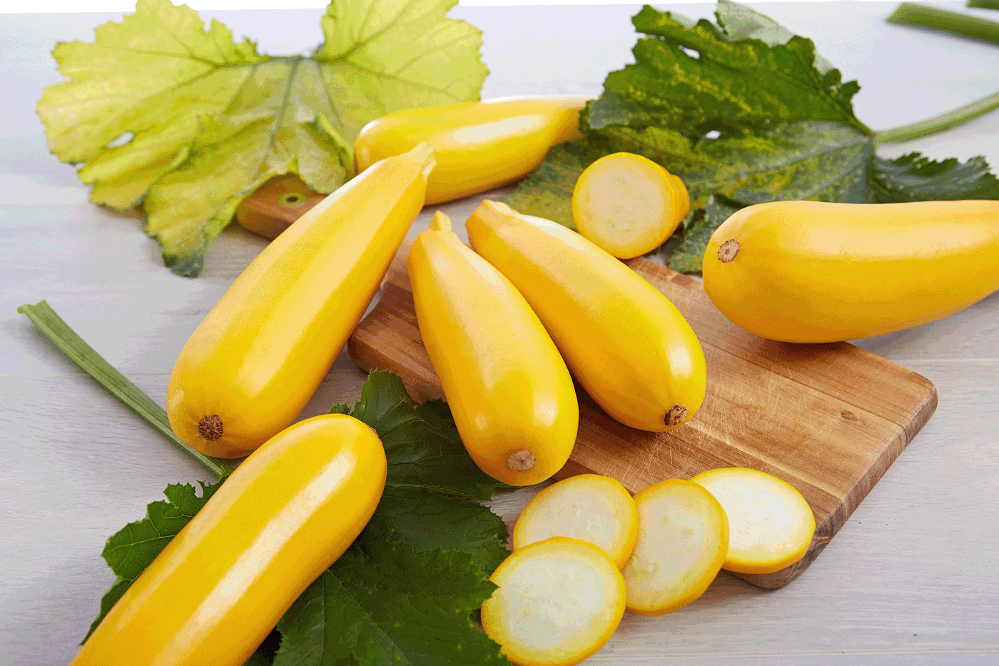 Haufen gelber Zucchini auf einem Holzteller mit grünen Blättern.