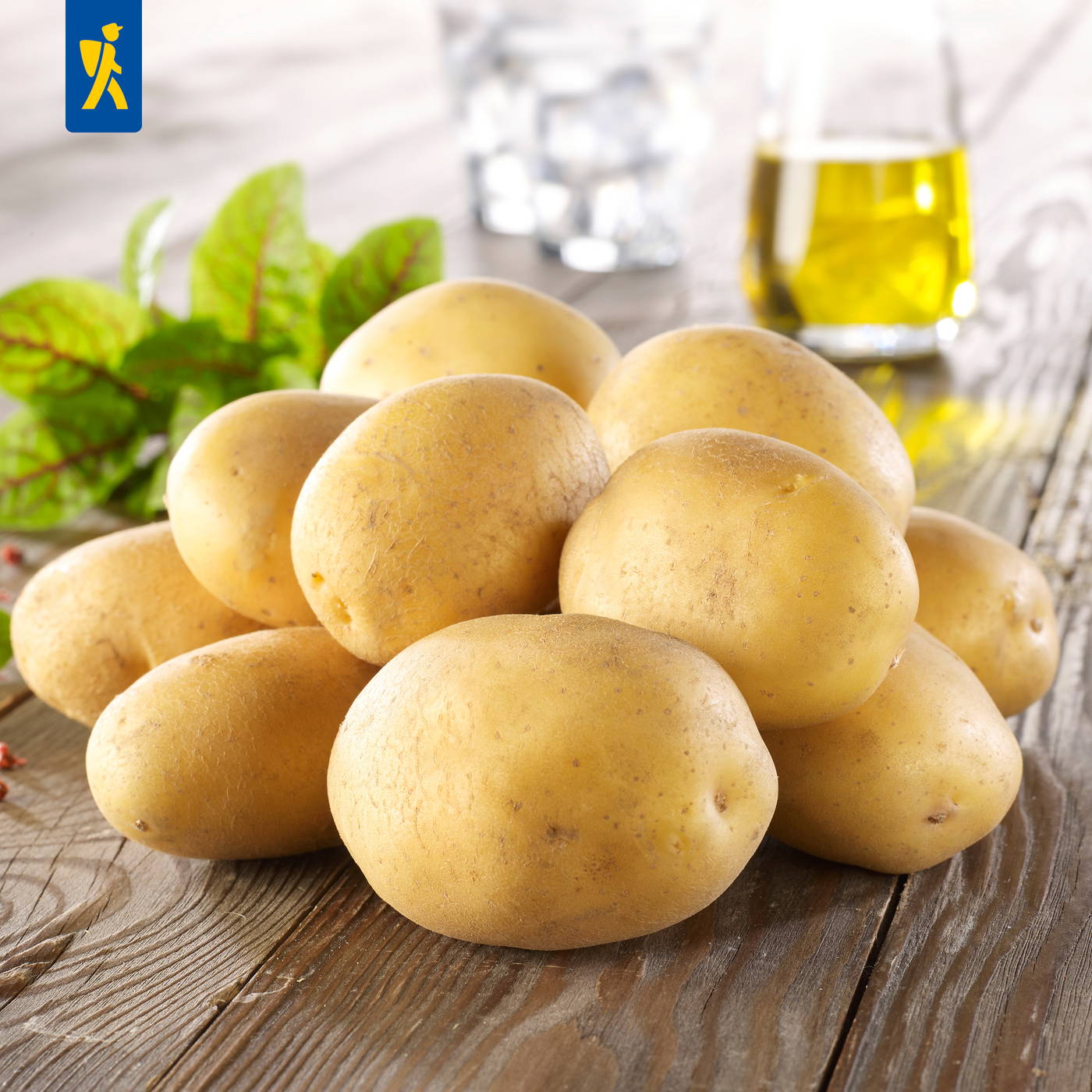 Haufen gelber Kartoffeln auf holz Tisch mit grünen Blättern, Glas Wasser und Öl im Hintergrund.