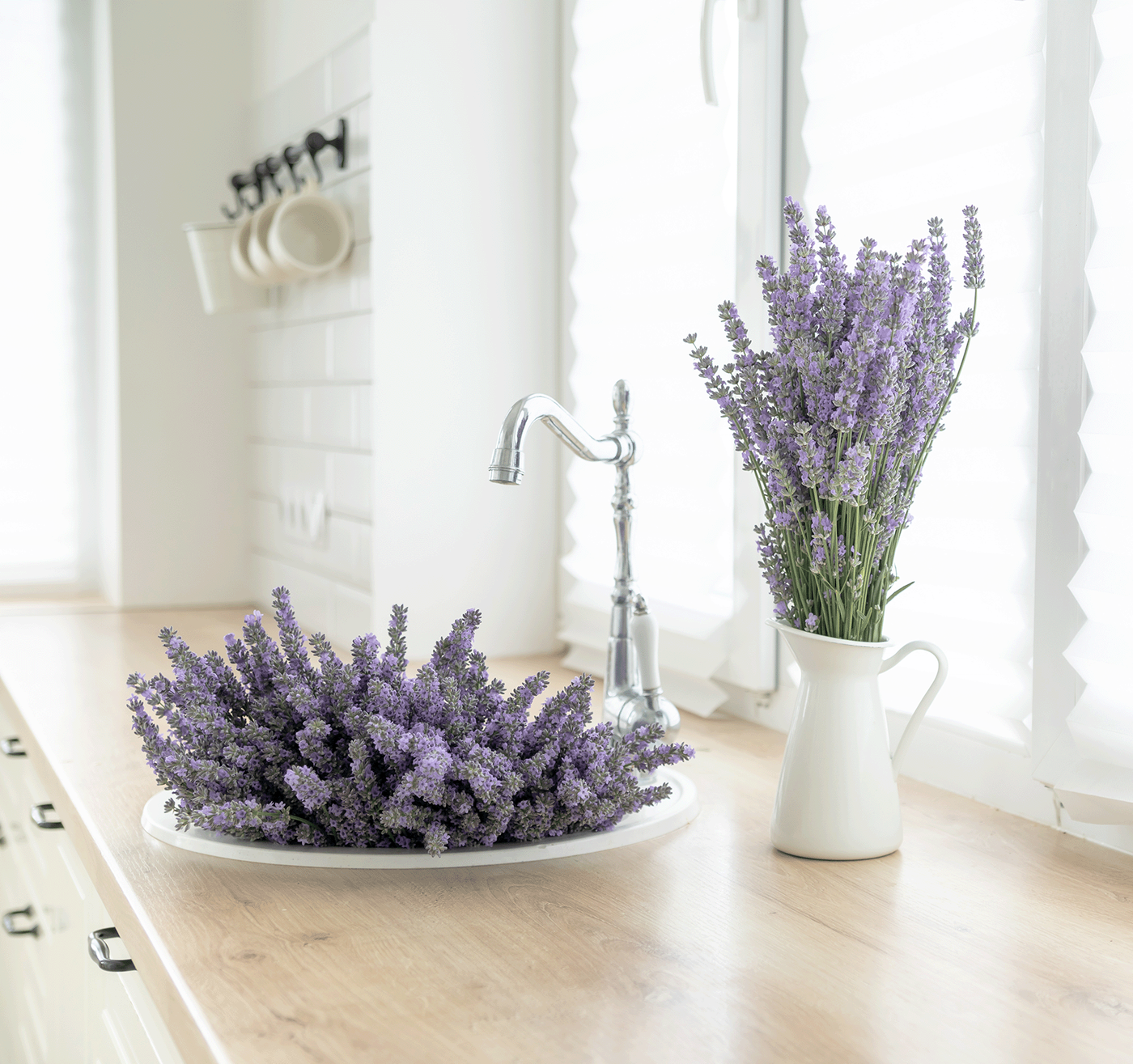 Vasen mit Lavendelblumen auf Holztisch vor weißen Fensterjalousien, Wasserhahn am Waschbecken.