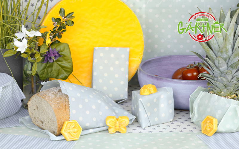 Gebundenes Brot, Geschenke, Obst, Blumen und Spielzeug vor Gartenthema mit Logo