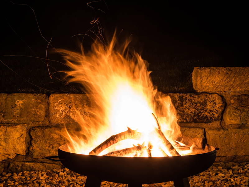 Lagerfeuer in einer Terrasse mit Steinmauer, offene Flammen und brennende Holzstämme.