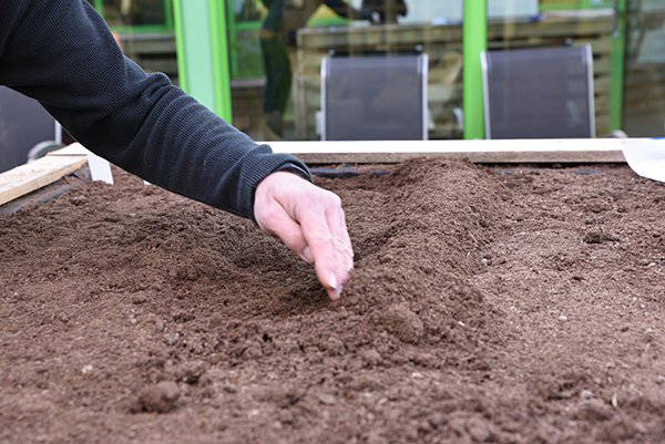 Hand streichelt Erde in Hochbeet vor Pflanzenanbau