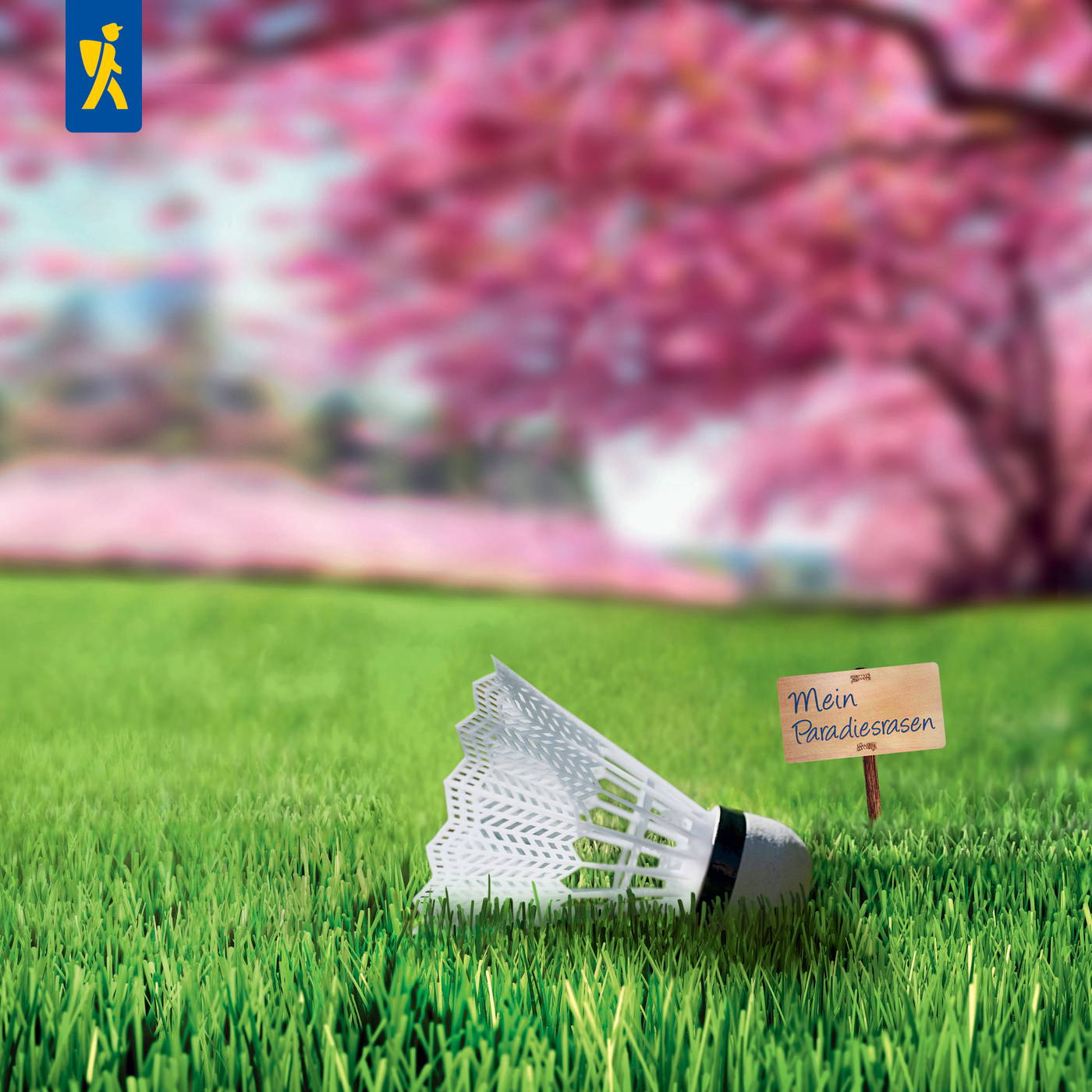 Badmintonschläger liegt auf grünem Gras neben einem kleinen Holzschild mit der Aufschrift "Mein Paradiesrasen".