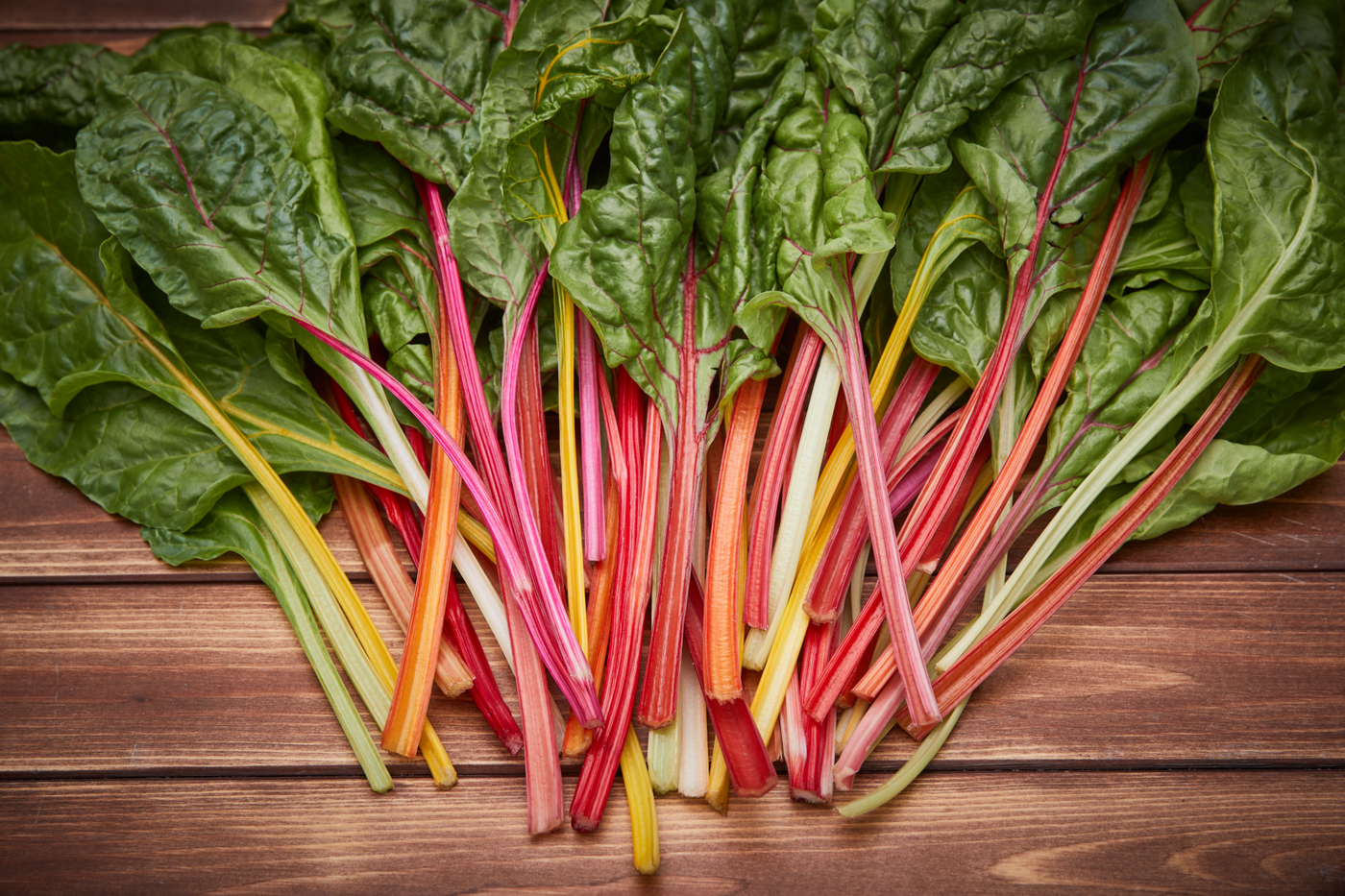 Bunte Rhabarberstängel mit grünen Blättern auf Holzuntergrund