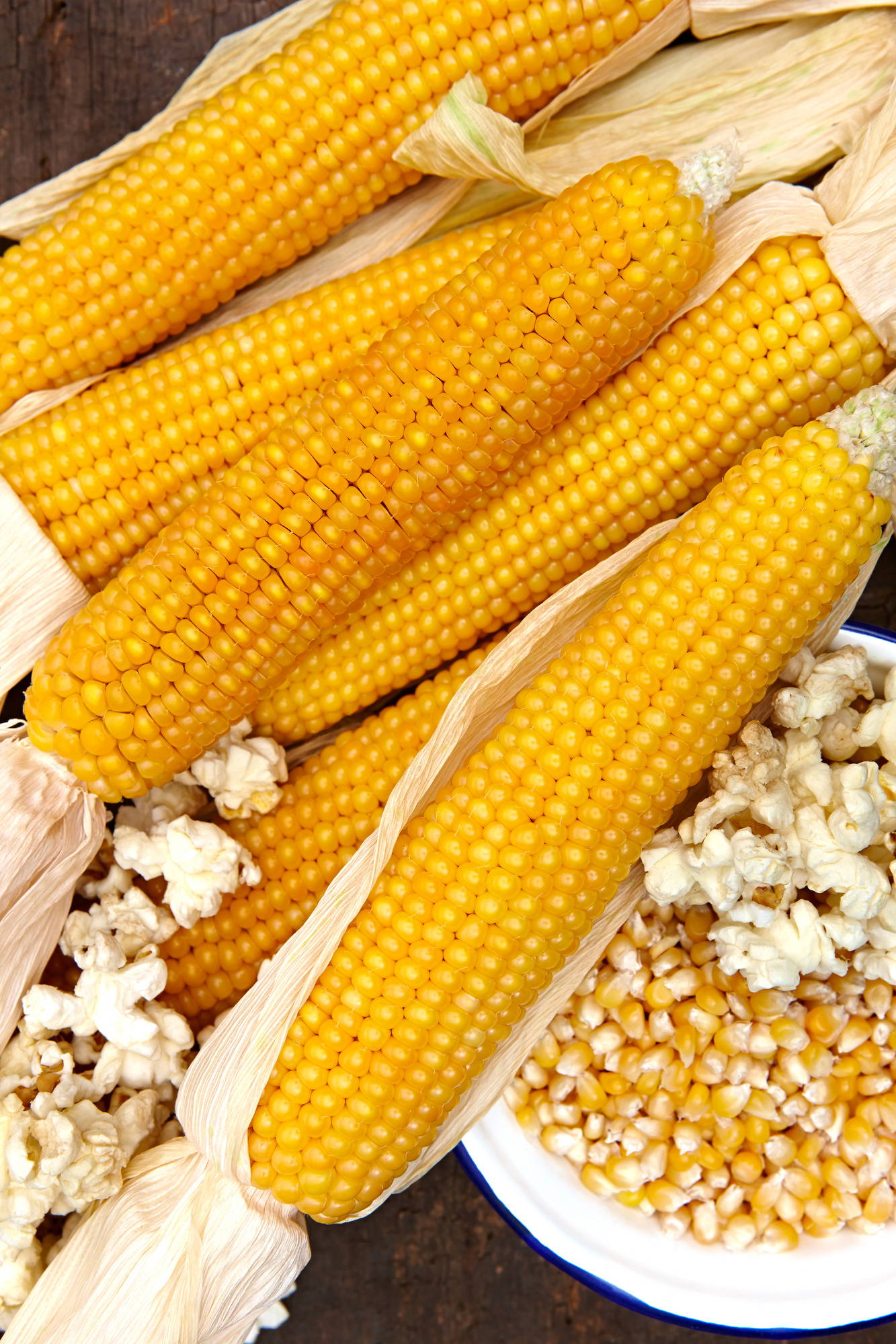 Maiskolben und gepoppter Mais in Schüssel auf Holzuntergrund
