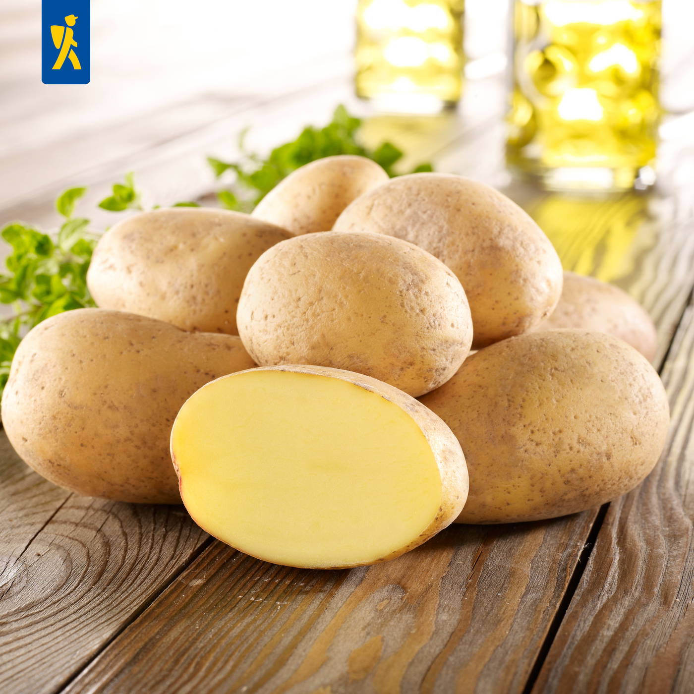 Mehrere rotschalige Kartoffeln, eine Hälfte geöffnet, auf einem Holzbrett mit grünen Kräutern im Hintergrund.