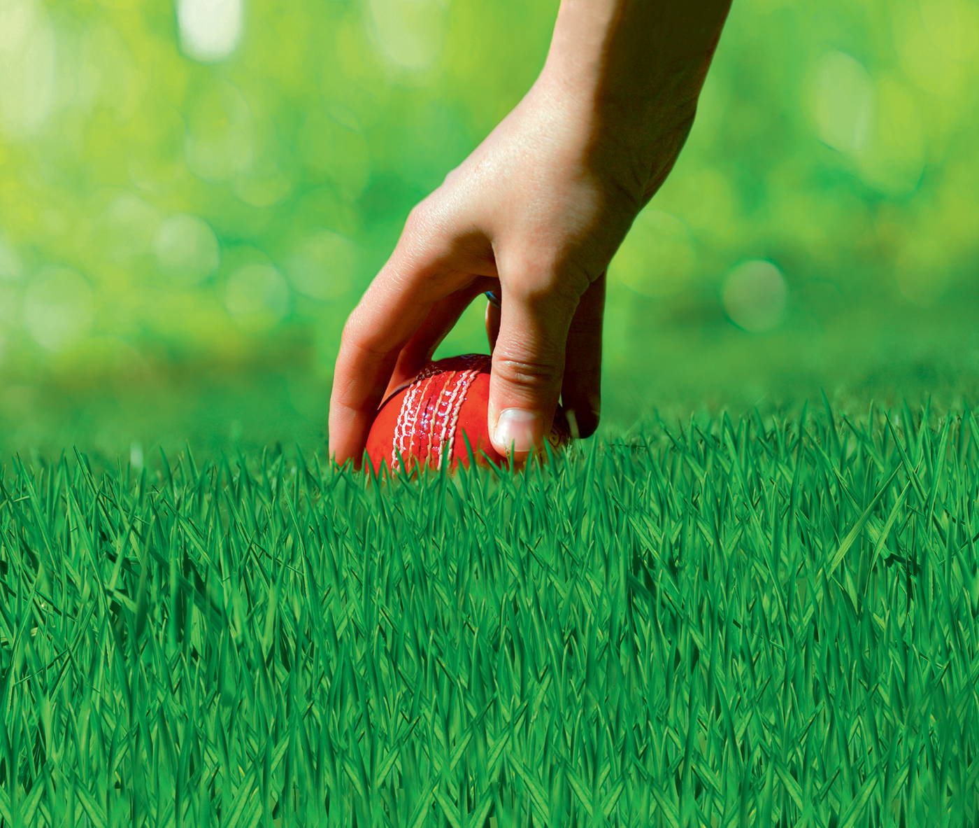 Hand legt einen roten Tennisball auf grünem Rasen.